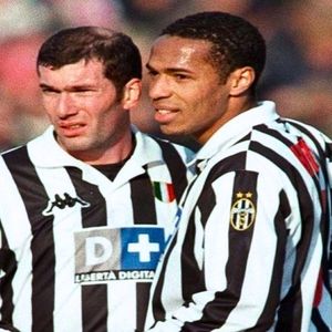 Zinedine Zidane and Thierry Henry standing side by side wearing the 1999 Juventus black and white striped football shirts, classic maillot style in the pitch stadium